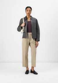 Graue übergroße Jacke mit Patchwork-Design, gerippter burgunderfarbener Oberteil, beigen, hochgeschnittenen Hosen und schwarzen Loafern. Schlichte Umhängetasche.
