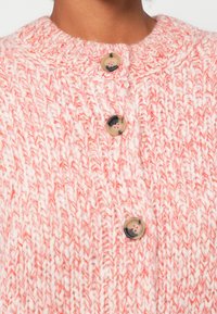 Jersey de punto grueso con hilo rosa y blanco, que presenta un cuello acanalado y tres botones redondos marrones en la parte delantera.