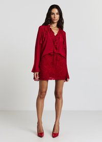 Blusa rossa con scollatura e maniche a volant abbinata a una mini gonna rossa a fantasia floreale. La modella indossa scarpe col tacco rosse coordinate.