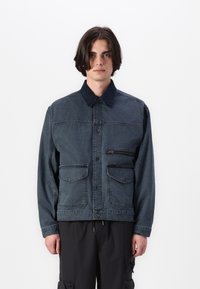 Dark blue denim jacket with a button-up front, two chest pockets, and a contrasting collar. The material has visible texture and stitching.