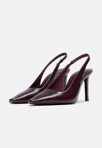 Burgundy patent leather slingback heels with pointed toe, thin stiletto heel, and textured upper. Open back design with ankle strap.