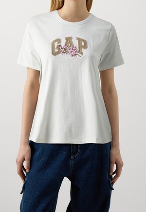 Witte katoenen T-shirt met het geborduurde "GAP" logo met bloemaccenten in roze en beige, ronde hals en korte mouwen.