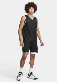 Svart atletisk tanktopp med hvit kant, kombinert med matchende svarte shorts med hvite striper. Stoffet virker lett og pustende.