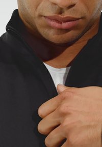 Black zip-up jacket with a high collar, featuring a textured fabric and a contrasting white undershirt visible underneath.