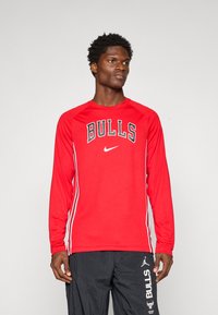Rød langærmet atletisk skjorte med "BULLS" og Nike-logo i sort, med hvide sidestropper og rund hals. Klar, letvægtsstof.