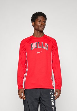 Chemise athlétique rouge à manches longues avec "BULLS" et logo Nike en noir, présentant des rayures blanches sur les côtés et un col rond. Tissu clair et léger.