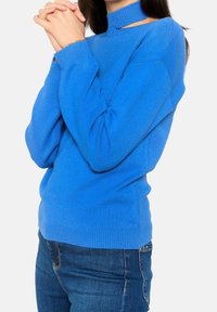 Pull tricoté bleu à col montant, avec des découpes latérales, manches longues et coupe décontractée. Associé à un jean bleu.