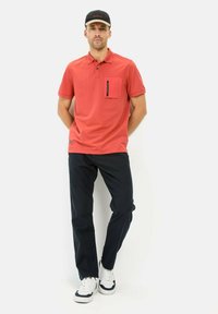 Rød polo-shirt med korte ærmer, knapkrave, enkelt brystlomme, parret med mørke bukser og hvide sneakers. Simpelt design, lavet af bomuldsstof.