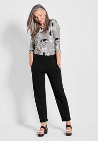 Zwarte op maat gemaakte broek met een relaxte pasvorm en plooien aan de voorkant, gecombineerd met een grijs topje met een geometrisch patroon in zwart en wit. Zwarte wedge sandalen.