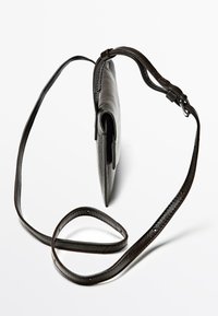 Svart läder crossover-väska med smidig yta, avlång form och justerbar rem. Har en minimalistisk design och ingen synlig hårdvara.