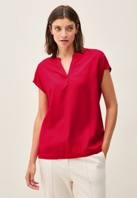Blusa rossa a maniche corte con scollatura a V e vestibilità rilassata. Tessuto morbido con una leggera lucentezza, caratterizzata da un orlo pulito e senza abbellimenti visibili.