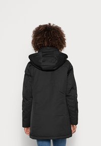 Sort isoleret jakke med hætte, lange ærmer og lige skæring. Har en glat tekstur og minimalistisk design uden synligt hardware.