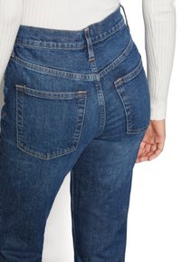 Džíny s vysokým pasem v tmavě modré barvě s hladkou texturou, se dvěma zadními kapsami a kontrastním prošitím podél švů.