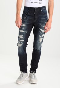 Tmavě modré džíny z denimu s distressed detaily, slim fit, pěti kapsami a zipem s unikátními kovovými akcenty.