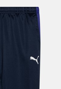 Mornarsko športno hlače z belim logotipom Puma, z enobarvnim dizajnom, elastičnim pasom in kontrastnimi vijoličastimi stranskimi akcenti.