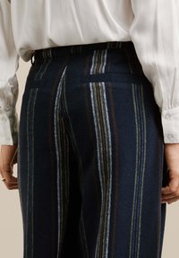 Pantalons en laine bleu marine avec des rayures verticales vertes, brunes et blanches. Dotés de deux poches arrière et d'une taille ajustée. Texture lisse.
