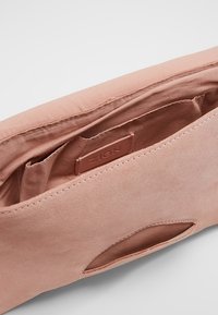 Borsa a tracolla in suede rosa con una texture liscia, dotata di una patch con logo all'interno e di un dettaglio con taglio su un lato. Contiene scomparti spaziosi.