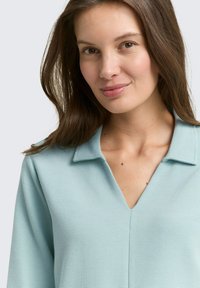 Himmelblause Bluse mit gerippter Textur, V-Ausschnitt und Kragen-Design. Glattes Material und figurbetonte Silhouette mit dezenten Details.