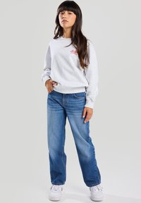 Harmaa huppari, jossa on pieni punainen logo, yhdistettynä sinisiin suoriin farkkuihin ja valkoisiin tennareihin, korostaen rentoa nykyaikaista tyyliä.