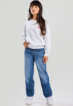 Light grey sweatshirt features a small red logo, paired with blue straight-leg jeans and white sneakers, highlighting casual contemporary style.