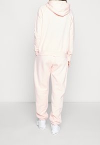 Ljusrosa hoodie och matchande mjukisbyxor i ett mjukt material, med ribbade muddar och en avslappnad passform. Sneakers med vita sulor.