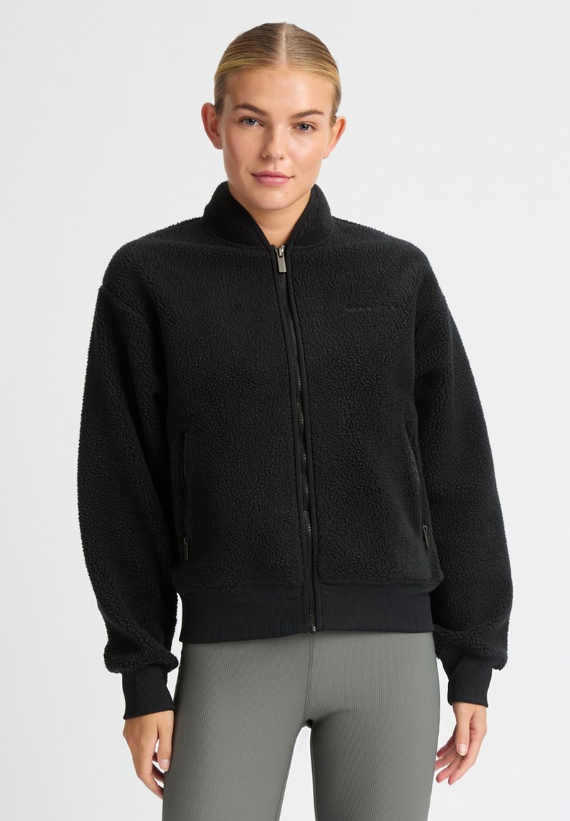 Chaqueta de forro polar negra con cuello alto, cierre de cremallera y puños acanalados. Cuenta con bolsillos laterales y una tela texturizada y mullida.