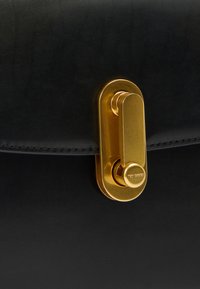 Melna ādas soma ar izceltu zelta metāla aizdari, gludu tekstūru un detaļām izšūtu maliņu.