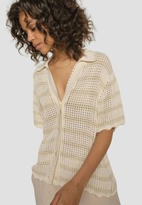Lightweight, open-knit cream cardigan with a collar, short sleeves, and button closure; features a subtle striped pattern.