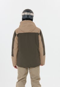 Giacca da sci con un design bicolore in olivo scuro e beige, dotata di cappuccio e materiale impermeabile. La vista posteriore mostra una silhouette elegante.