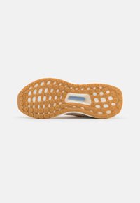 Semelle de chaussure avec une semelle extérieure en caoutchouc brun clair dotée de motifs circulaires d’adhérence et d’un insert central bleu "TORSION SYSTEM".