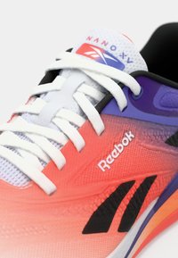 Reebok Nano X1 apaviem ir gradienta rozā uz oranžu virsma, melni akcenti, balti auklas un teksturēts sieta dizains. Logo ir redzams.