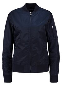 Marinblå bomberjacka tillverkad av slät nylon. Har en dragkedja fram, ribbad ärmslut, sidofickor och en ficka på armen med dragkedja.
