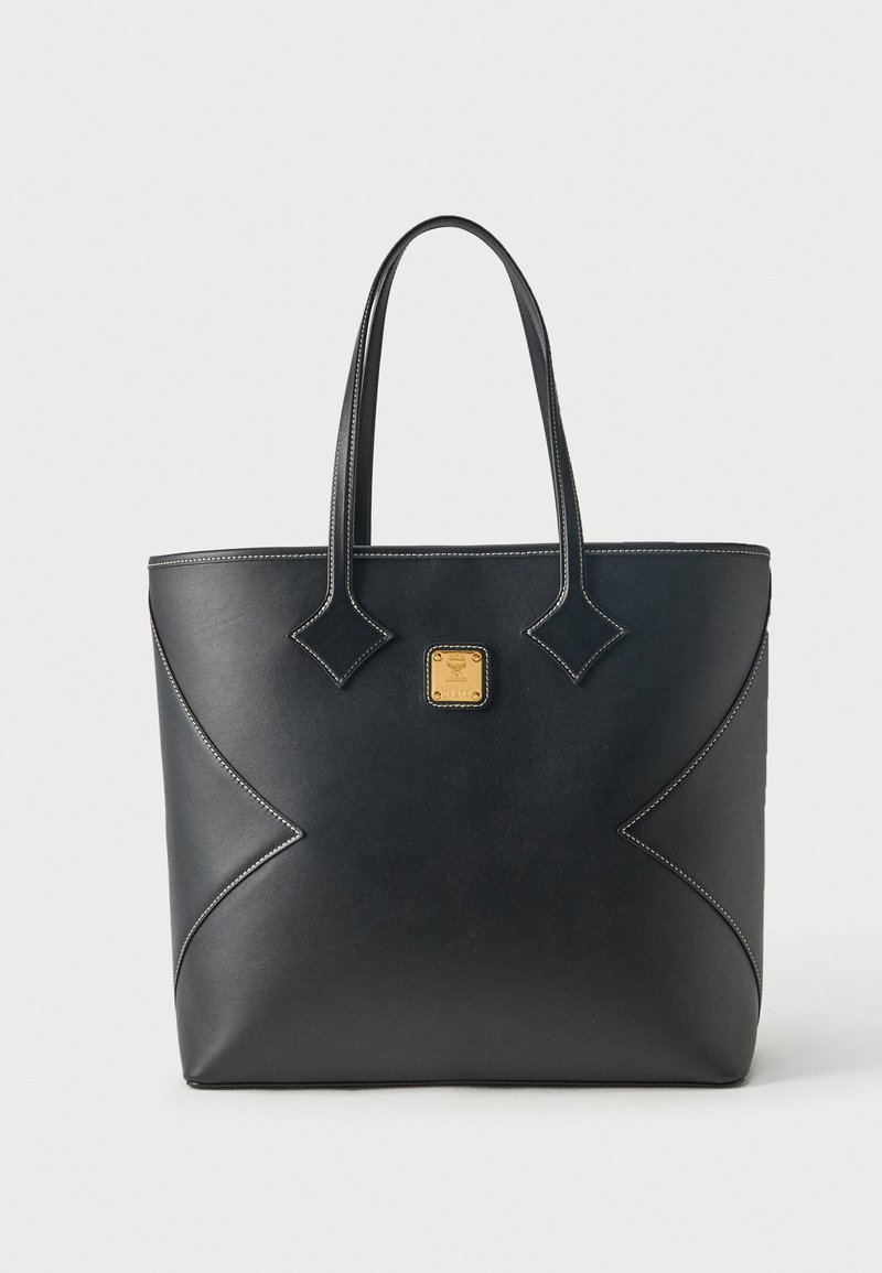 Sac cabas en cuir noir avec doubles poignées, coutures blanches et un petit emblème carré doré centré sur le devant.