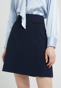 Navy blue skirt with a textured fabric, fitted waist, and side pockets with black trim. Paired with a light blue, silky blouse.