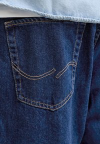 Close-up of blue denim jeans back pocket with orange stitching and light blue fabric above the pocket.