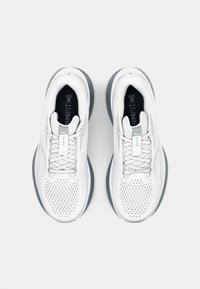 Baskets de sport blanches avec une tige en maille, semelles en caoutchouc grises et lacets plats. Les caractéristiques comprennent des perforations pour la respirabilité et un logo discret.