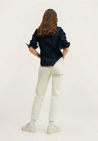 Camisa de mezclilla oscura con mangas enrolladas, pantalones crema claros ajustados y zapatillas blancas con suelas grises. Diseño sencillo, sin patrones visibles.