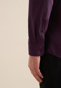 Paarse langemouwen shirt met een zachte textuur, twee knopen op de manchetten en een klein geborduurd rozendetail.