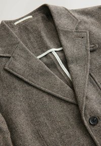 Brown herringbone blazer with a notched lapel, single button closure, textured fabric, and contrasting inner lining. Black button detail visible.