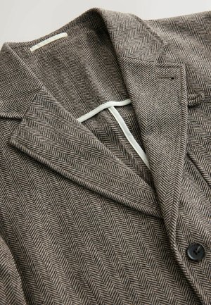 Brązowa marynarka w jodełkę z wyłogami, jedno guzikiem, teksturowanym materiałem i kontrastową podszewką. Widoczny czarny guzik.