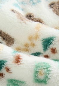 Hvid fleece tæppe med blød tekstur, prydet med spredte teal, brun og tan pletter i forskellige størrelser over stoffet.