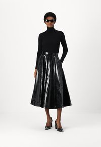 Suéter de cuello alto negro con текстura acanalada, falda de cintura alta plisada en material negro brillante con textura de cocodrilo, combinada con zapatos de tacón alto negros.