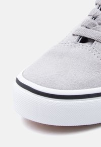 Γκρι σουέντ αθλητικό παπούτσι με υφή στο πάνω μέρος, λευκή λαστιχένια σόλα και  μαύρη διακοσμητική γραμμή. Διαθέτει μπροστινό κορδόνι και ελάχιστες ραφές.