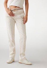 White patterned trousers with a lightweight fabric, featuring a floral design in beige, elastic waistband, and drawstring for adjustable fit.