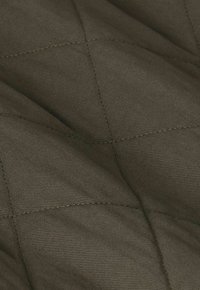 Donkergroen doorgestikt quiltstof met vierkant stikselpatroon en zichtbare textuur en plooien.