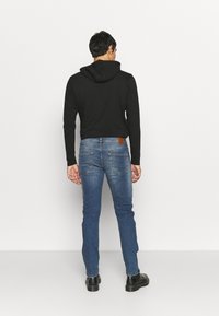 Sudadera negra con capucha, diseño ajustado. Combinada con vaqueros azules de mezclilla que cuentan con una etiqueta de cuero marrón y un estilo de cinco bolsillos. Botas negras.