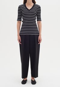 Svart och vit randig kortärmad topp med V-ringning, kombinerad med svarta vida byxor och svarta slip-on skor.