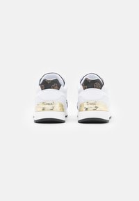 Zapatillas blancas con una textura suave, detalles dorados en el talón y un interior oscuro con un patrón. Punta redonda y suela plana de goma negra.
