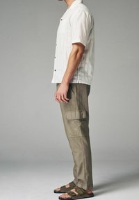 Hvid kortærmet skjorte med knapper, lodrette striber og brystlomme; olivengrønne cargobukser med sidelommer; sorte sandaler med to remme.