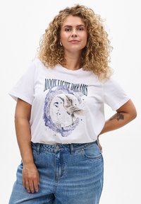 Weißes Baumwoll-T-Shirt mit einem grafischen Design eines Mondes, eines Vogels und dem Text "MOON LIGHT DREAMS" in Grün, kombiniert mit blauen Jeans.